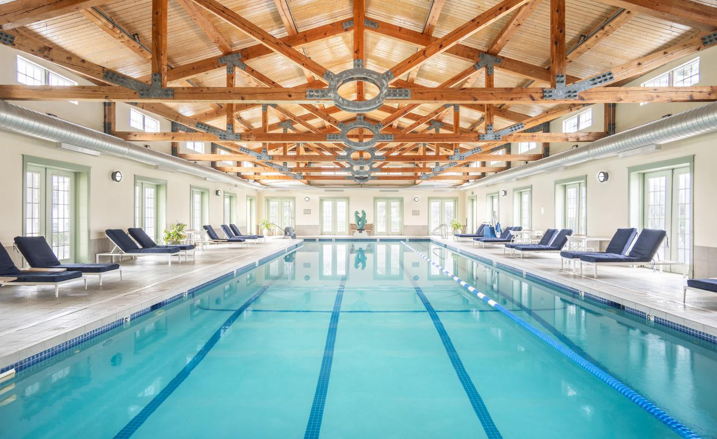 Indoor swimming pool with blue lanes, lounge chairs, and exposed wooden beams