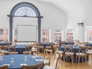 Elegant banquet hall with round tables, blue linens, and tall arched windows