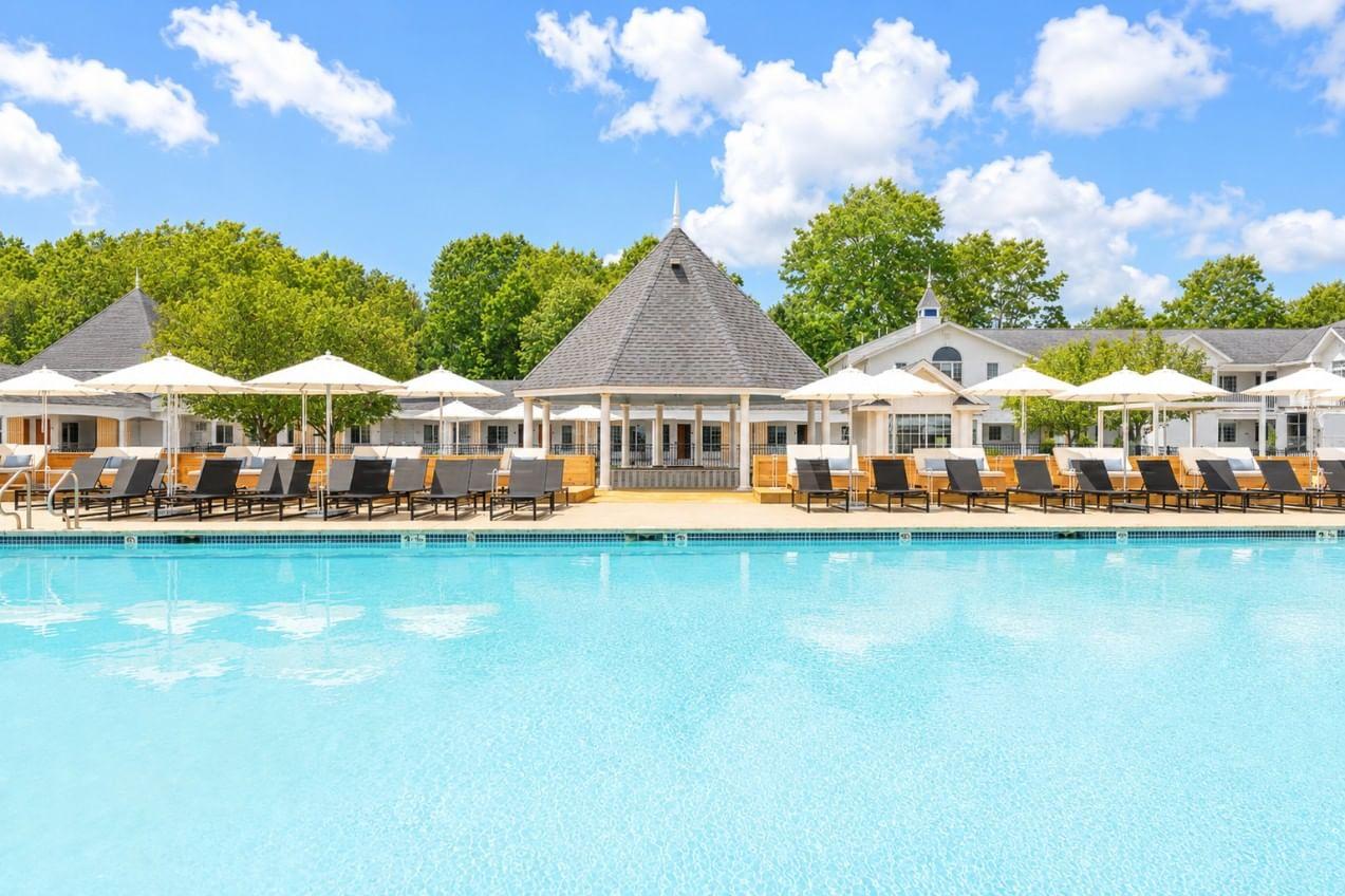 Resort pool with lounge chairs and thatched-roof villas under a blue sky