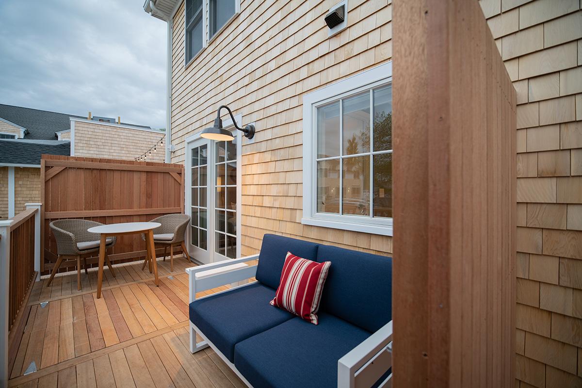Small wooden deck with a navy sofa, red striped pillows, and outdoor dining table.