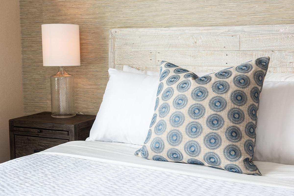 Neatly made bed with patterned blue pillow, bedside lamp, and wood-paneled wall