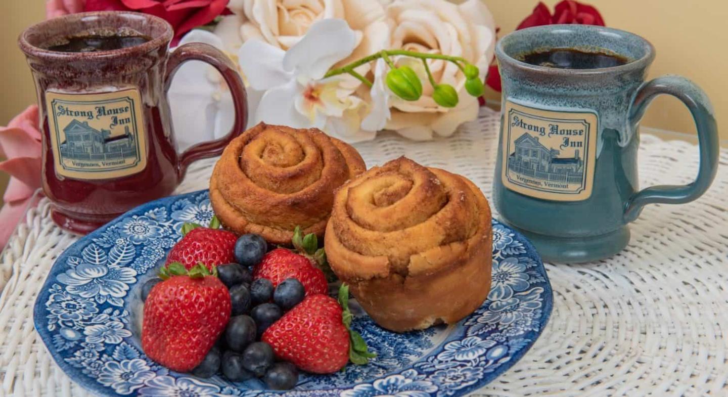 Blueberry muffins, cinnamon rolls, and fresh berries on patterned plates with tea mugs.