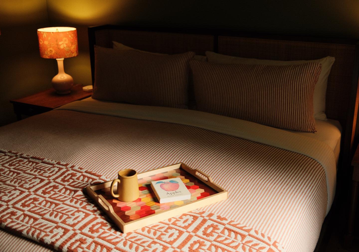 Cozy bedroom with a made bed, warm lamp, and breakfast tray.