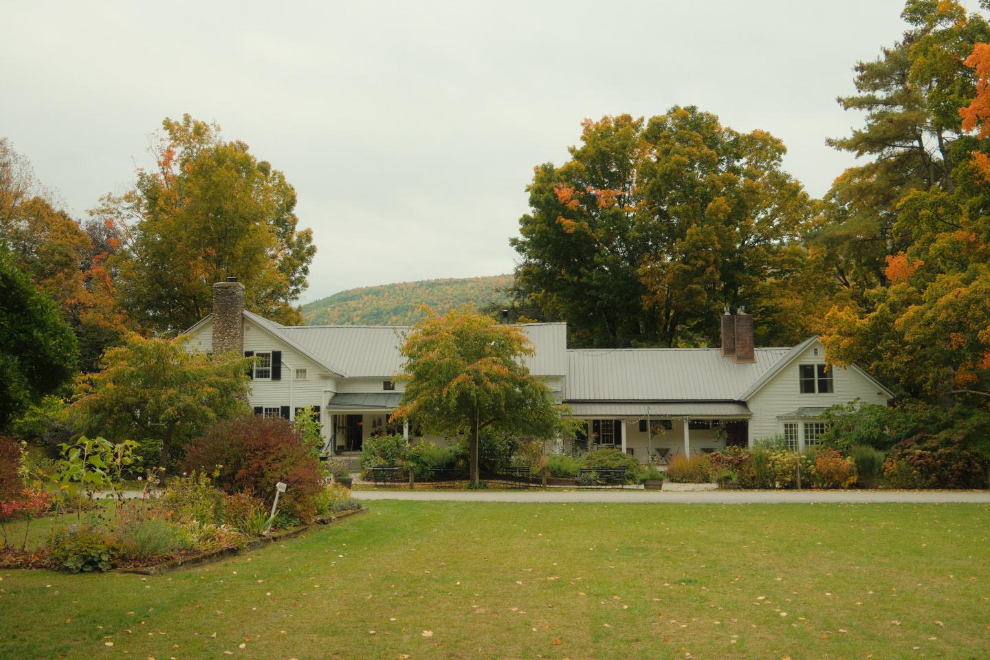 White farmhouse surrounded by autumn trees and a wide green lawn