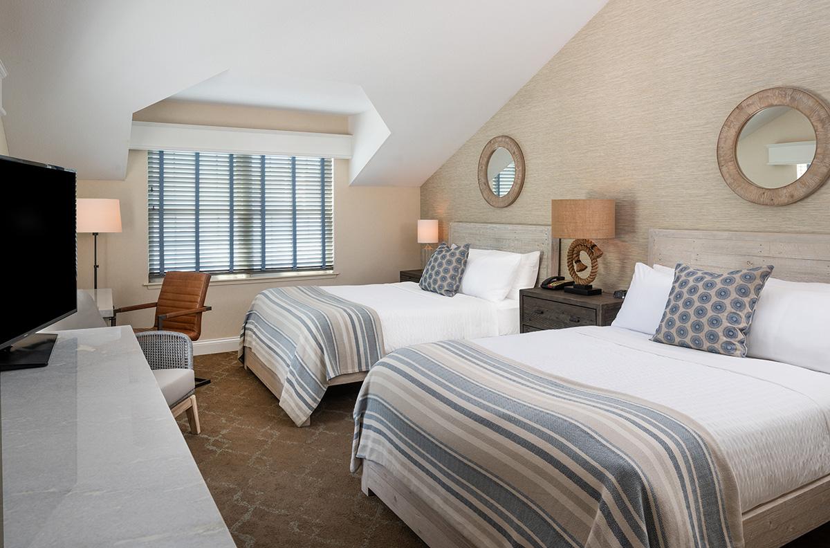 Bright bedroom with two striped twin beds, blue accents, and a large wall mirror.