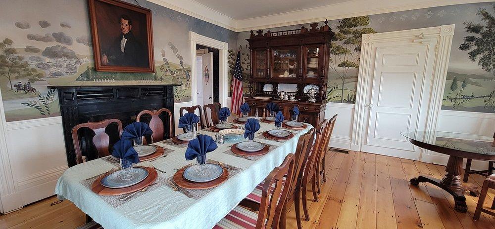 Dining room with a blue-and-white set table, antique furniture, and mural wallpaper.