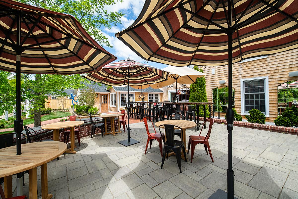 Outdoor restaurant patio with striped umbrellas, wooden tables, and chairs.