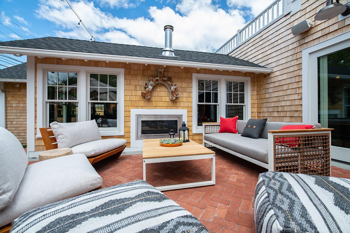 Cozy brick patio with white sofas, striped cushions, fireplace, and blue sky.