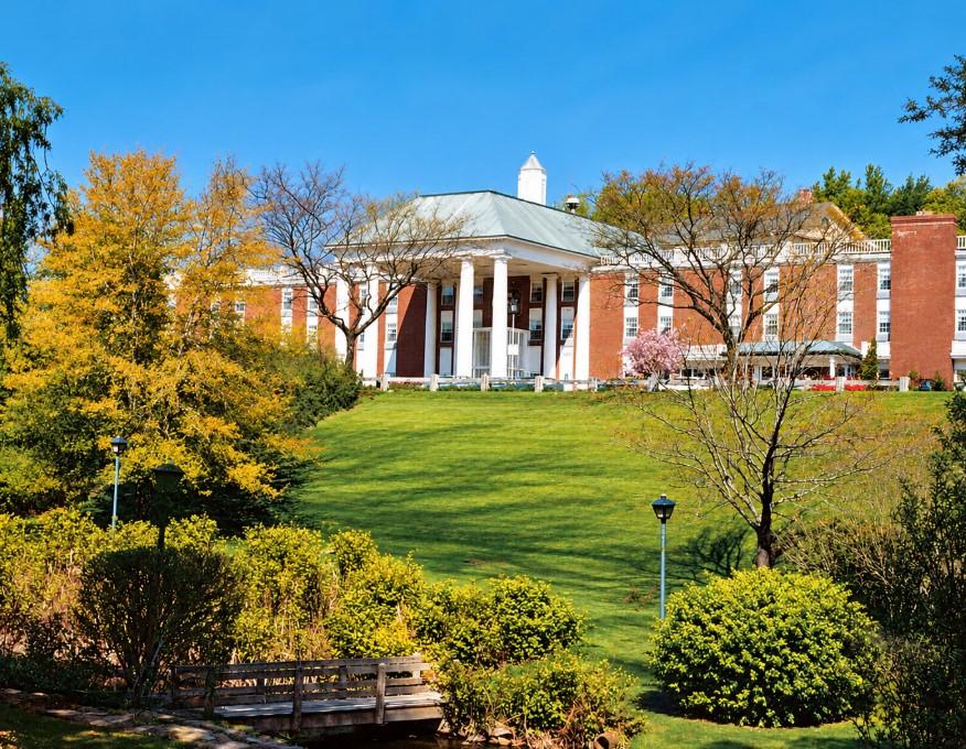 Red-brick colonial building with white columns amid colorful autumn trees.