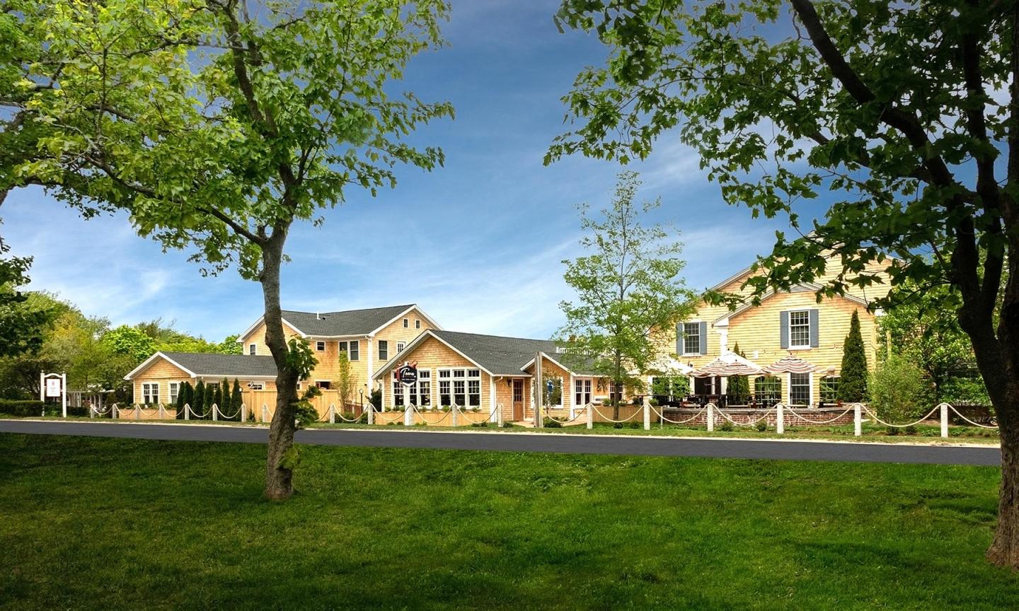 Large country house with a green lawn and trees under a blue sky.