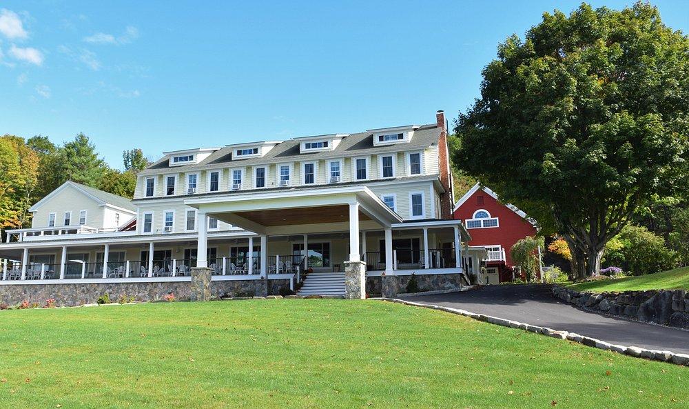 Large white colonial-style inn with a wraparound porch on a green lawn.