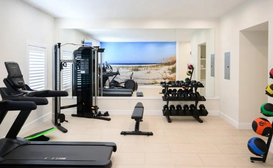 Bright home gym with treadmill, weight bench, dumbbells, and exercise equipment.
