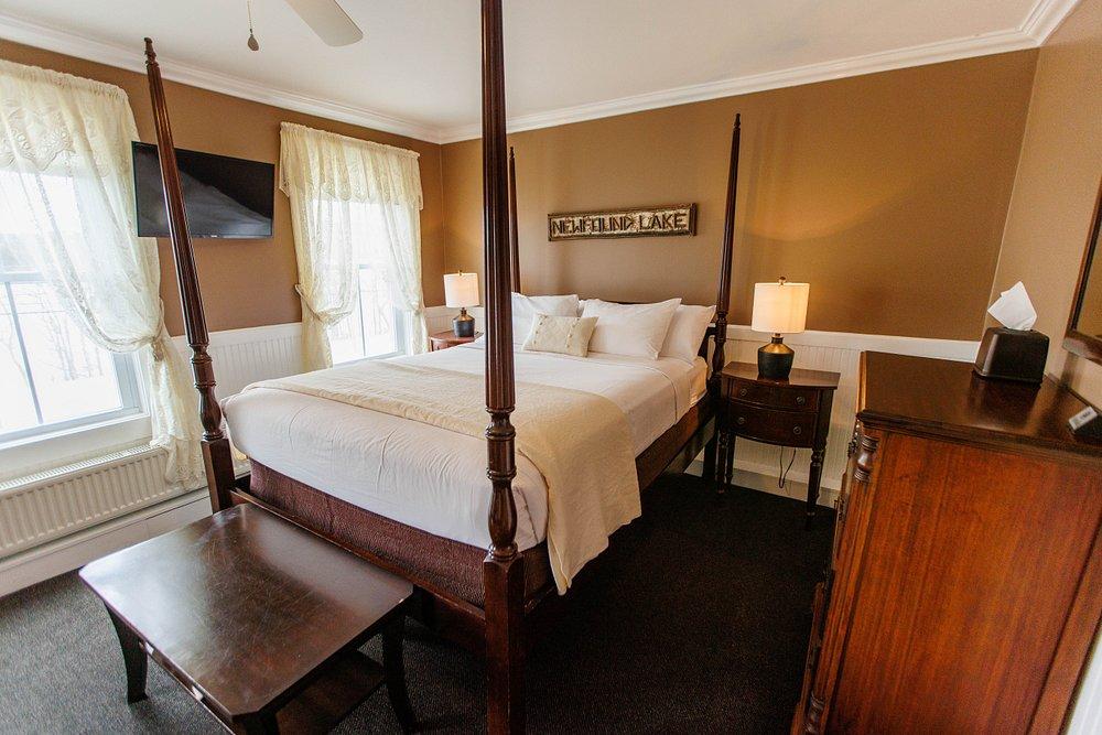 Cozy hotel bedroom with four-poster bed, dark wood furniture, and warm beige walls.