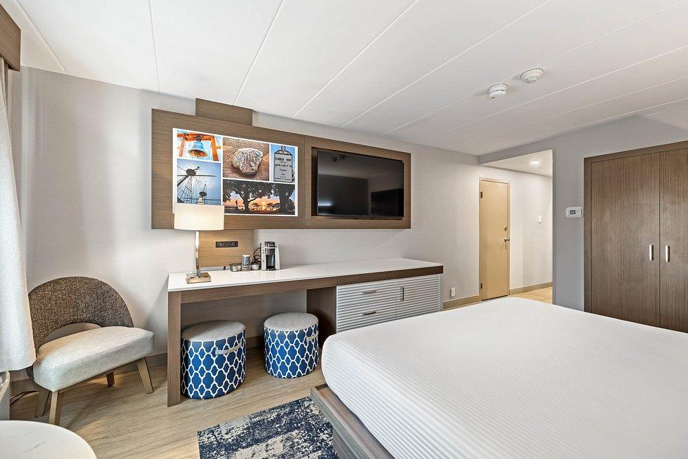 Modern hotel room with king bed, seating area, TV, and blue patterned stools.