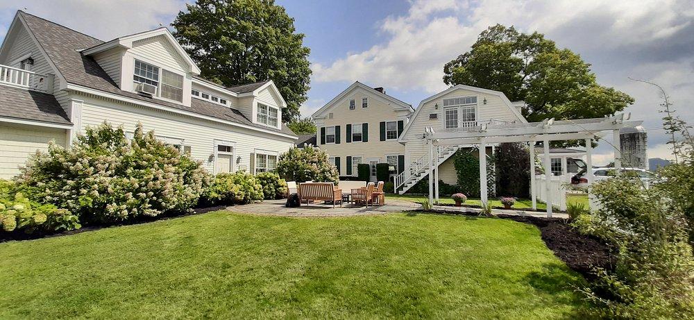 Large green lawn between white suburban houses under a partly cloudy sky.