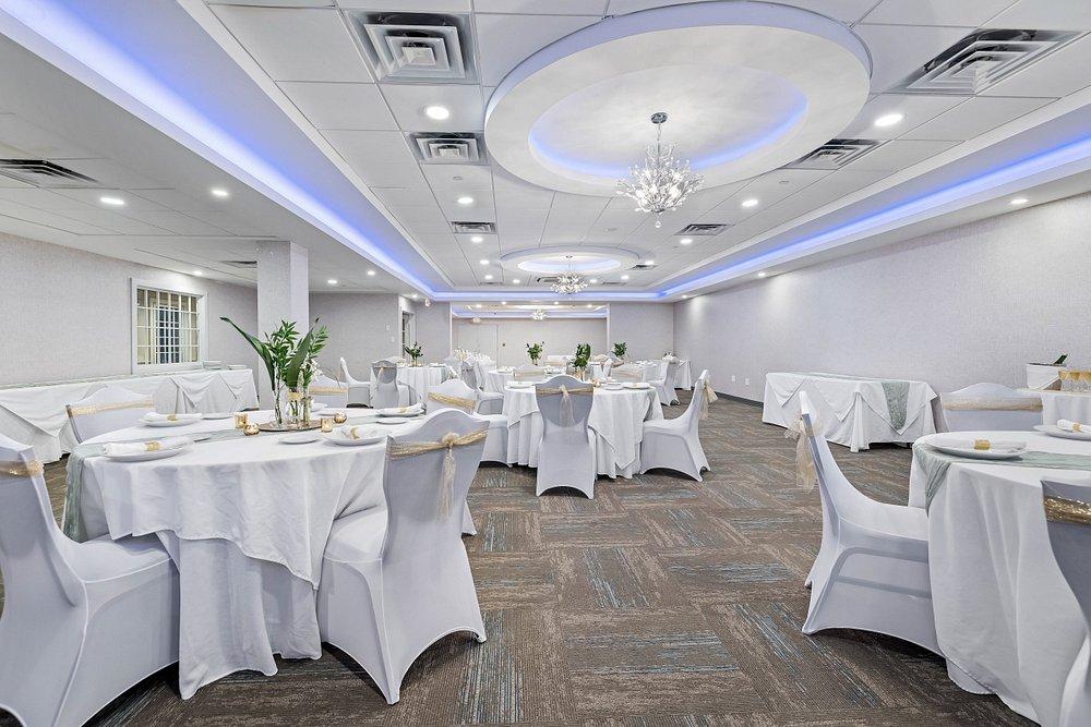 Elegant banquet hall with round tables, white chair covers, and blue ceiling lighting.