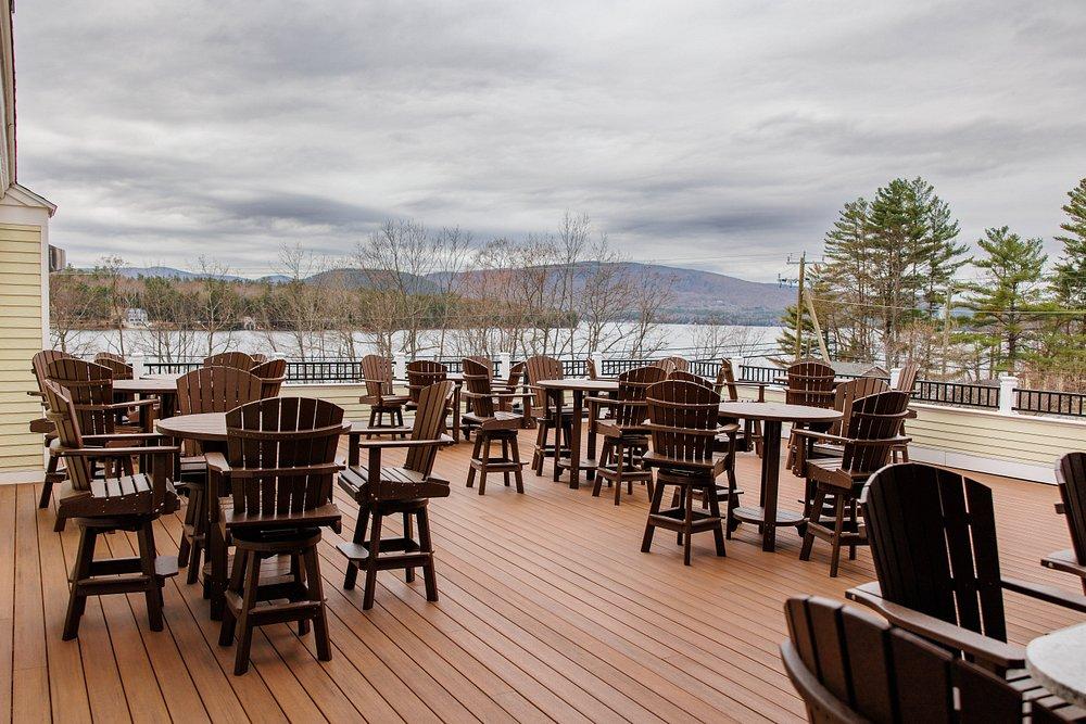 Empty wooden patio dining area overlooking a lake under cloudy skies.