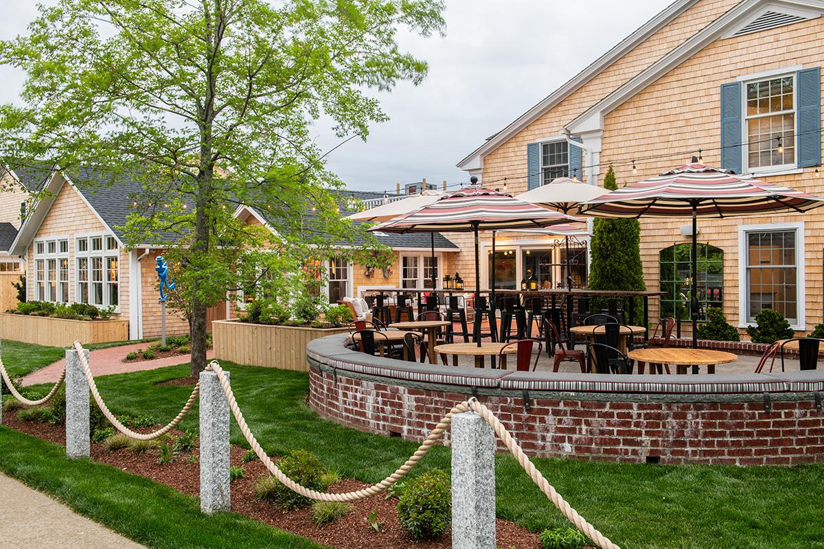 Outdoor patio dining beside a yellow house, bordered by rope posts and greenery.