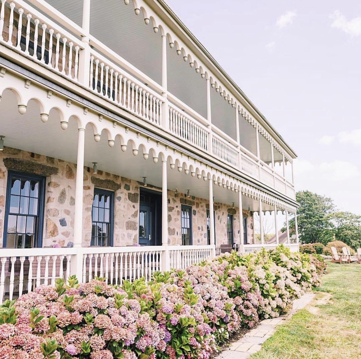 Historic two-story veranda with white railings and blooming pink hydrangeas
