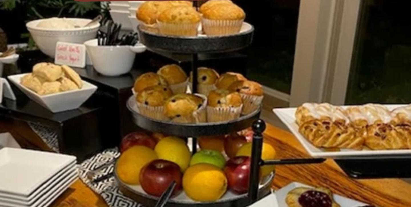 Tiered buffet display with muffins, fruit, pastries, and desserts.