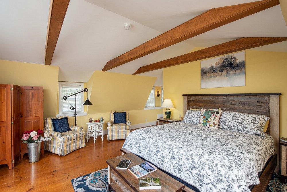 Cozy attic bedroom with exposed beams, patterned bed, and wooden floors.