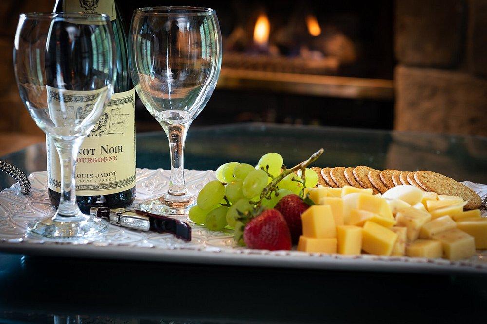 Wine, cheese, grapes, and crackers on a platter by a fireplace.