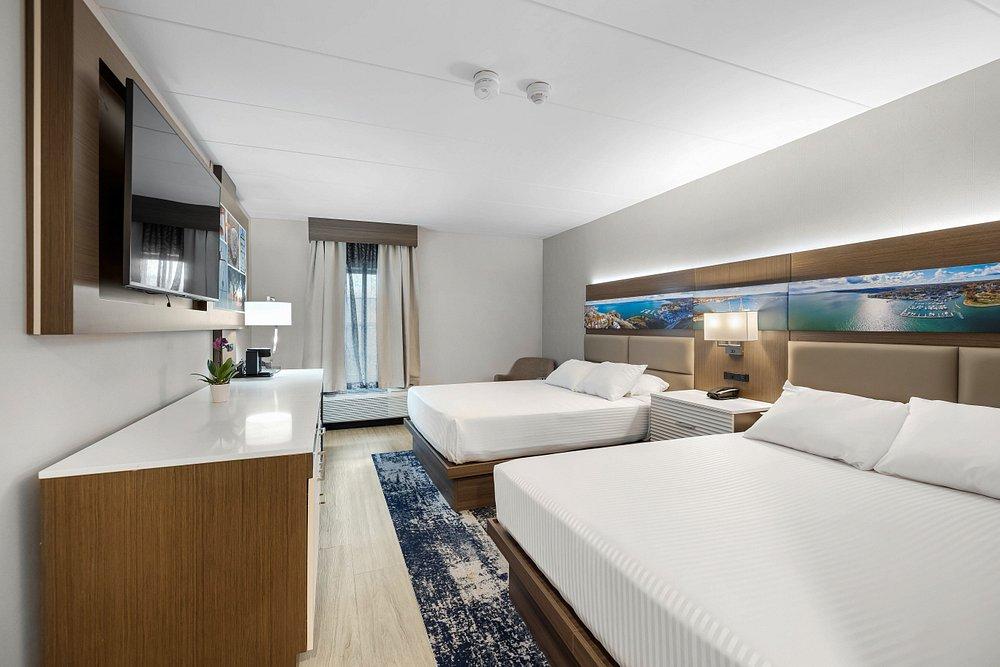 Modern hotel room with two beds, wood cabinetry, and a city-view window.