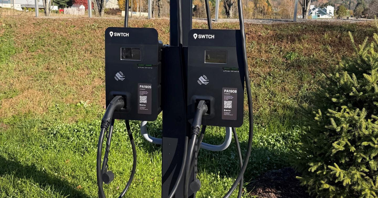 Two black electric vehicle charging stations beside a grassy roadside.