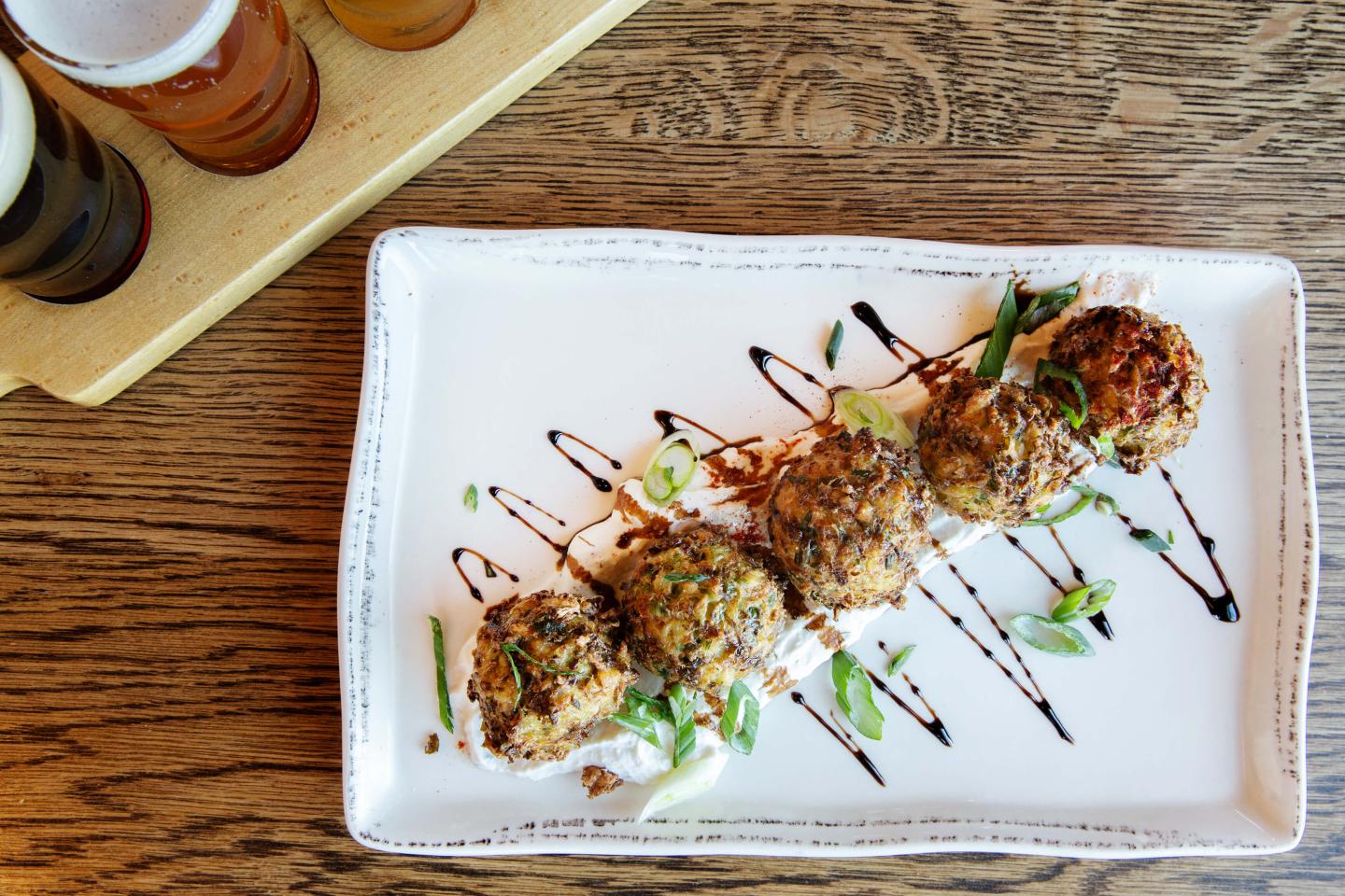 brussel sprout fritters covered in balsamic glaze with a flight of beers on wooden table