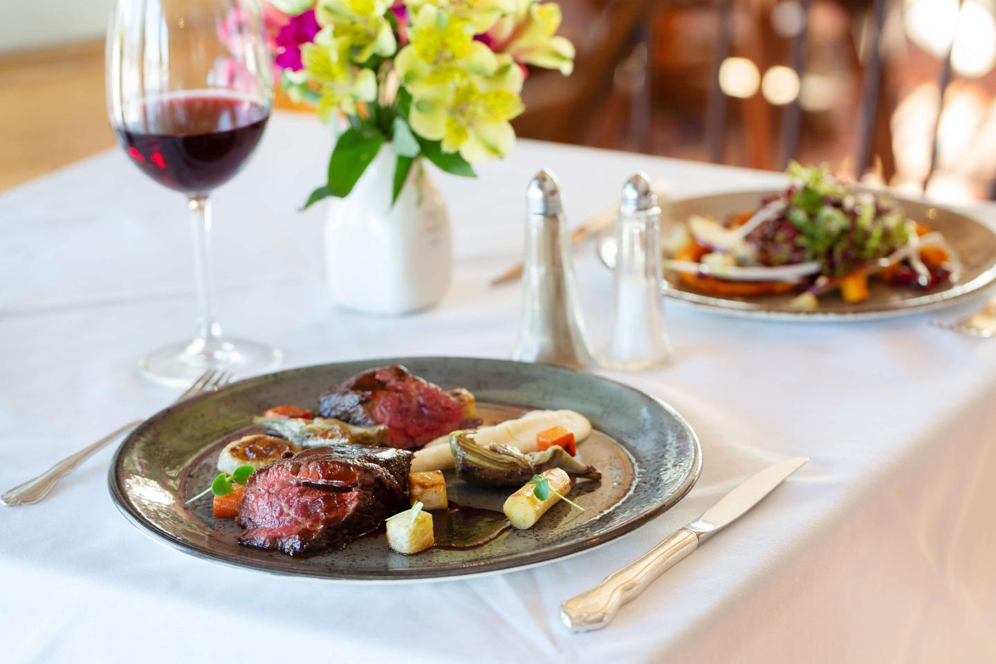 meat and vegetables on plate with flowers and wine set