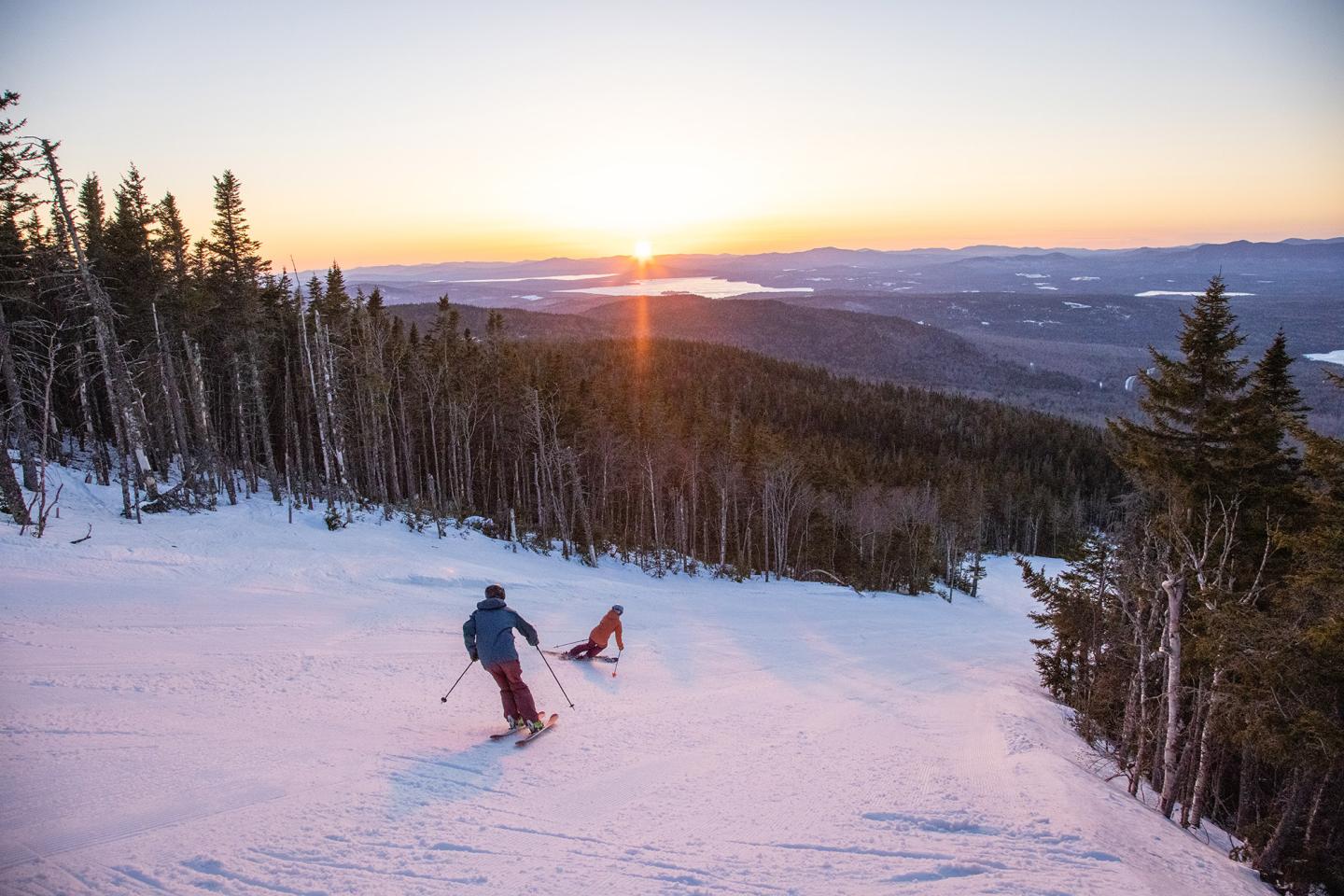 Scenic view of skiers at sunset down a groomed run