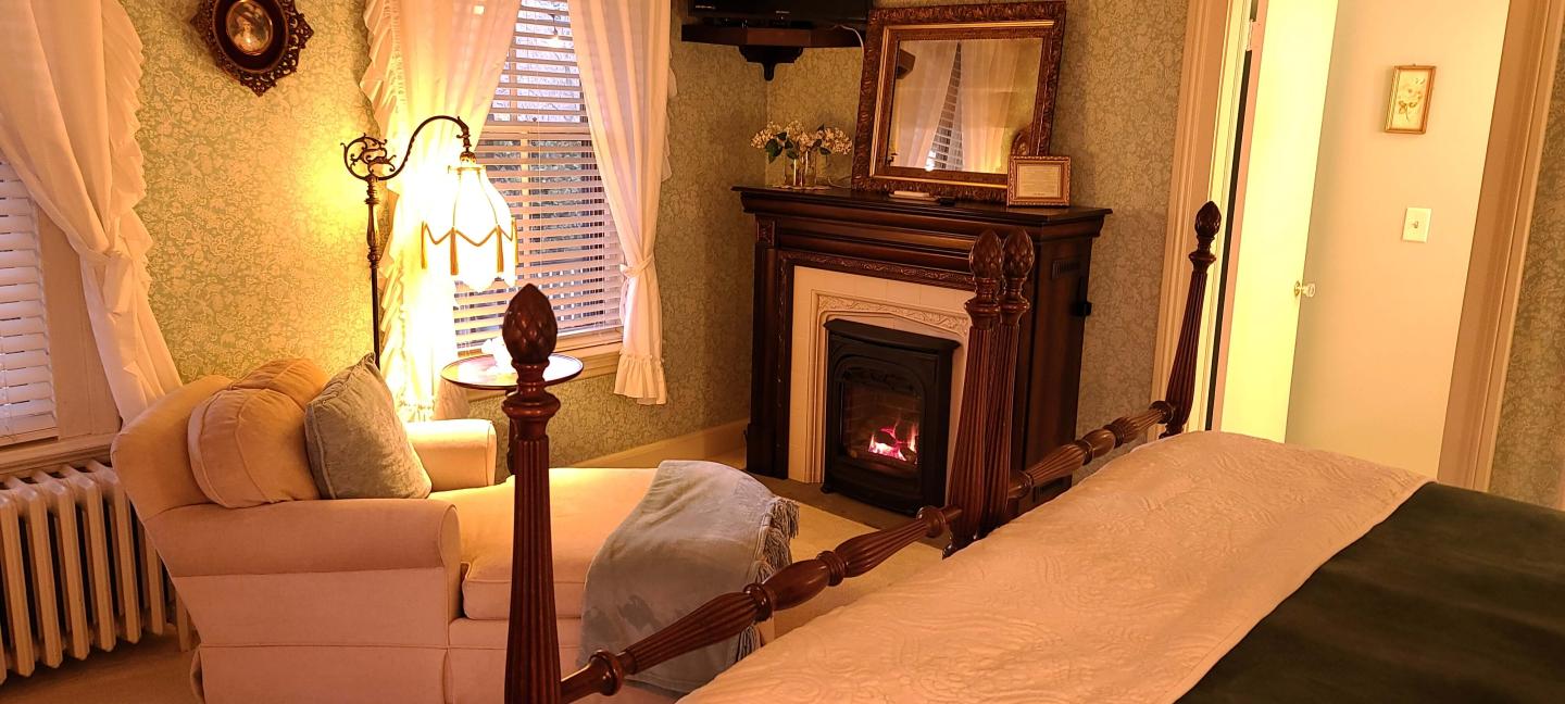 A lit fireplace creates a cozy atmosphere in a comfortable room with a king bed and chaise lounge.