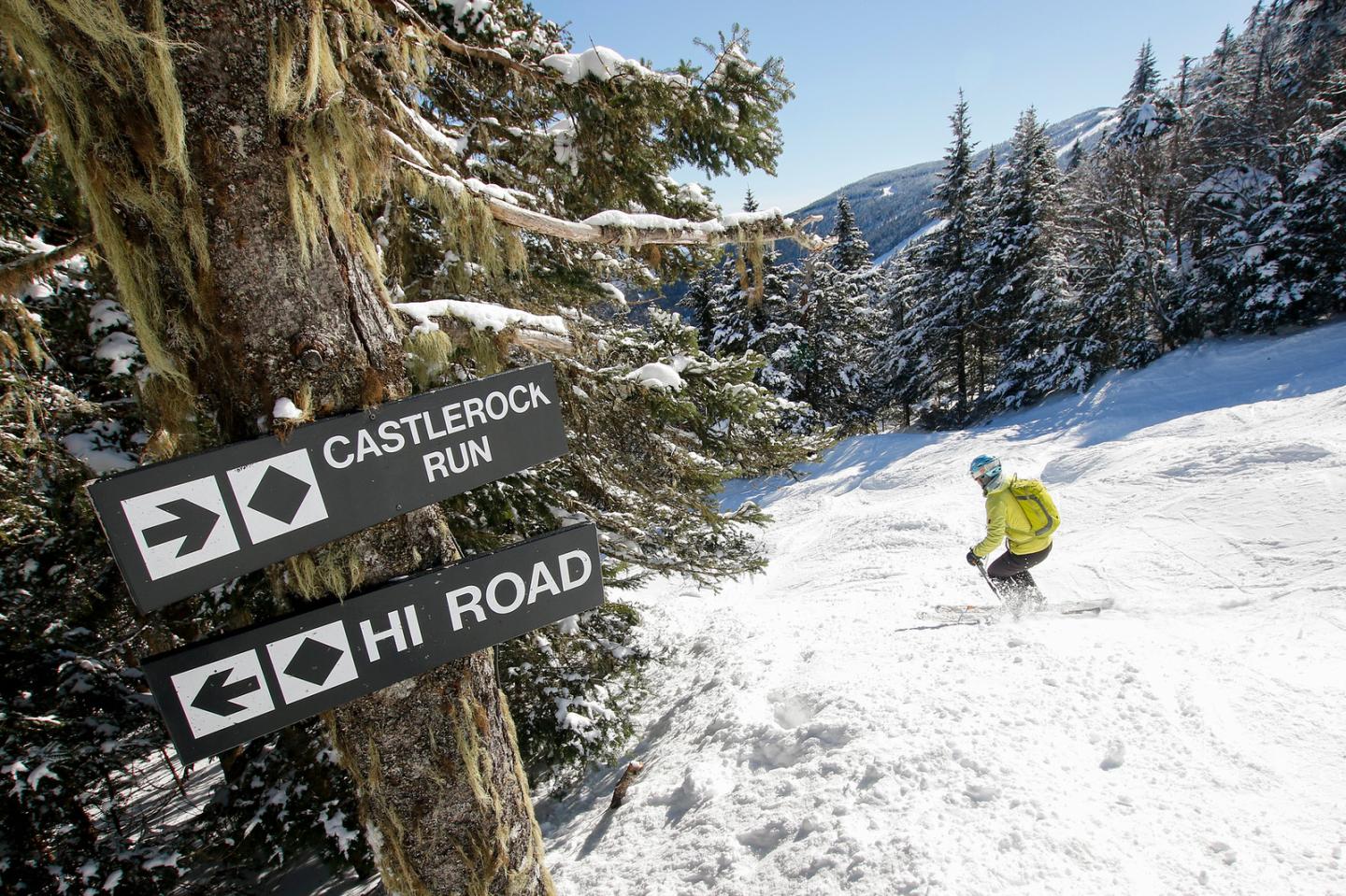One skier on steep terrain with trail sign in foreground