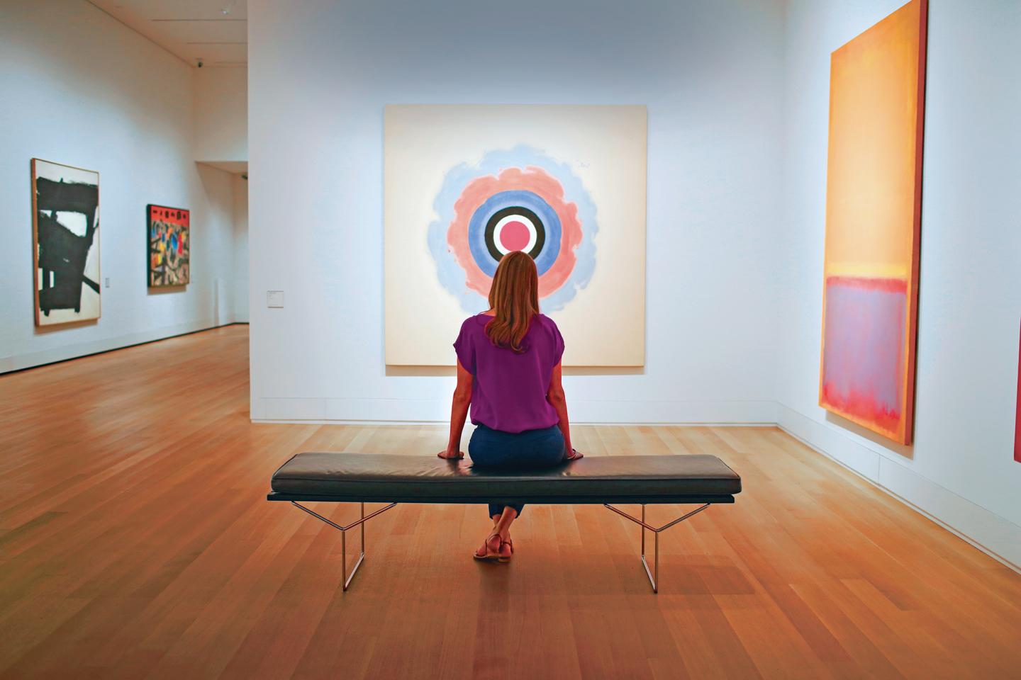 Single person sitting on a bench at an art museum viewing a painting