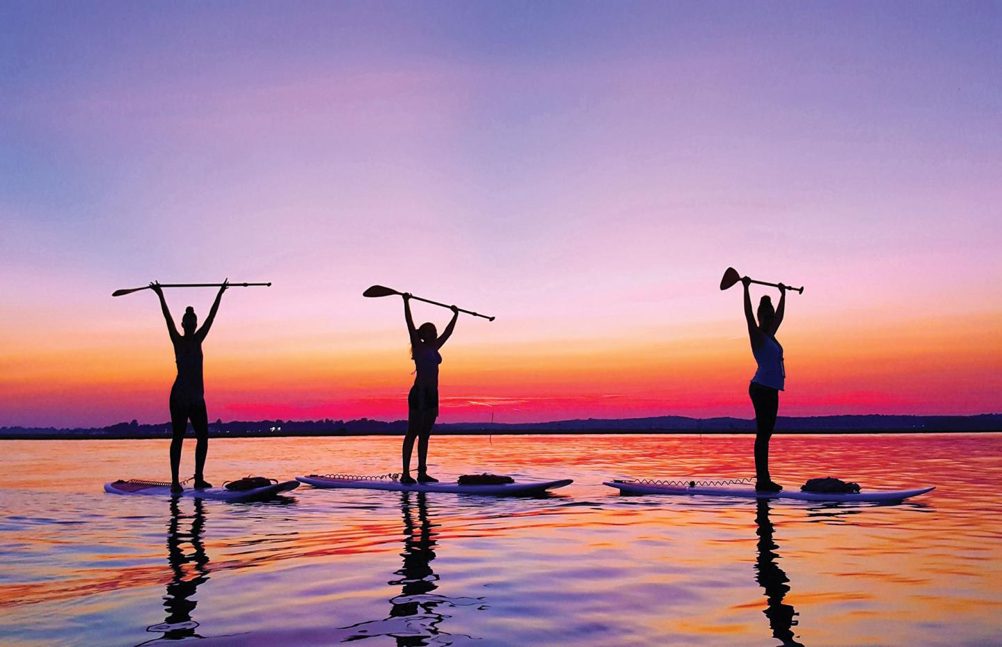 Three paddle boarders on the water at sunset