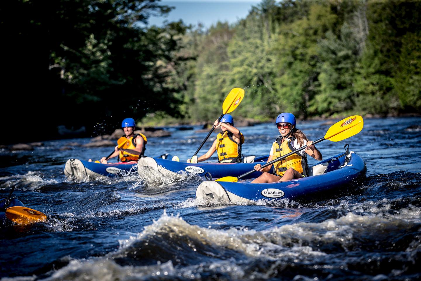 Three kayakers in white water with yellow oars