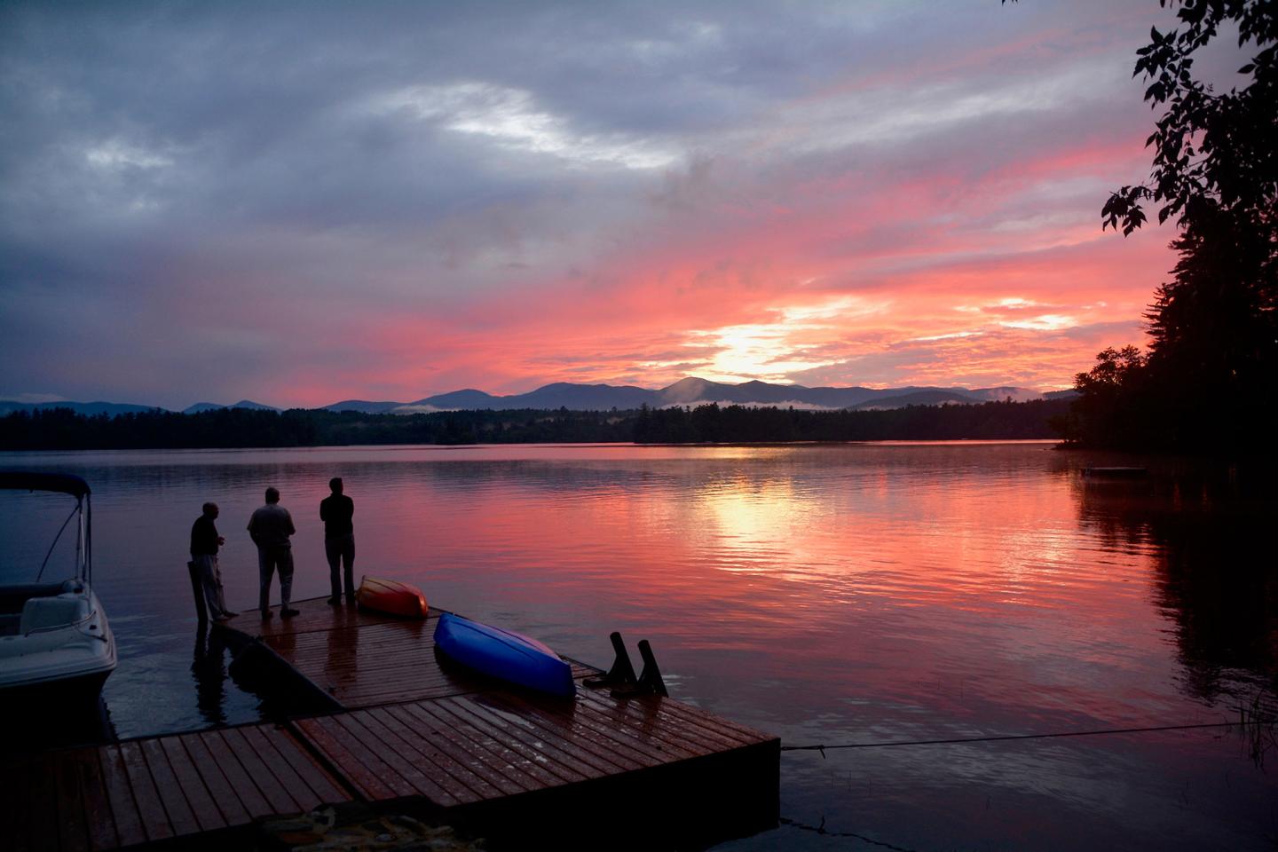 Three people on a dock watching the sunset