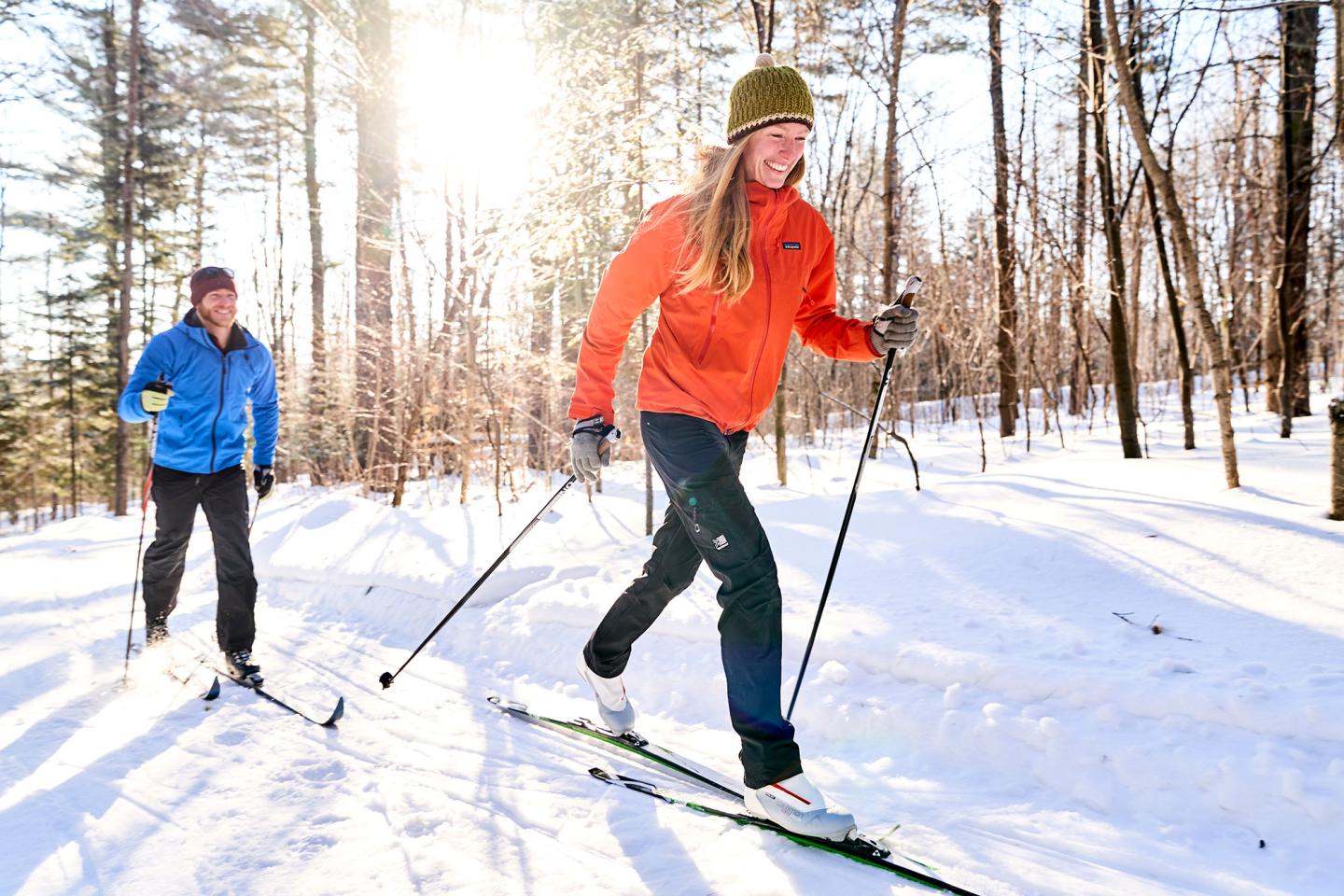 Two people cross country skiing through the trees