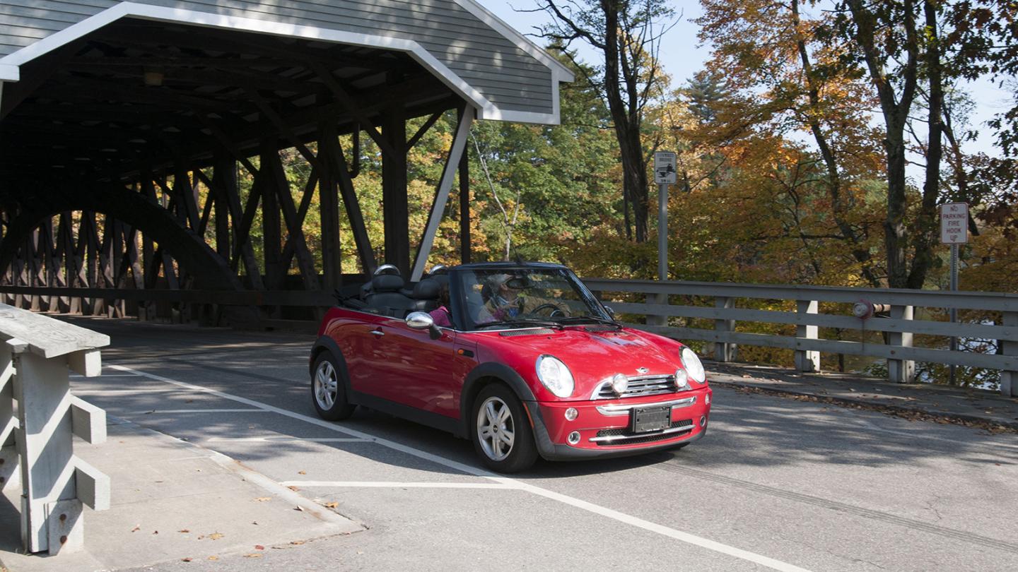 Red car driving through covered bridge with fall leaves in the background