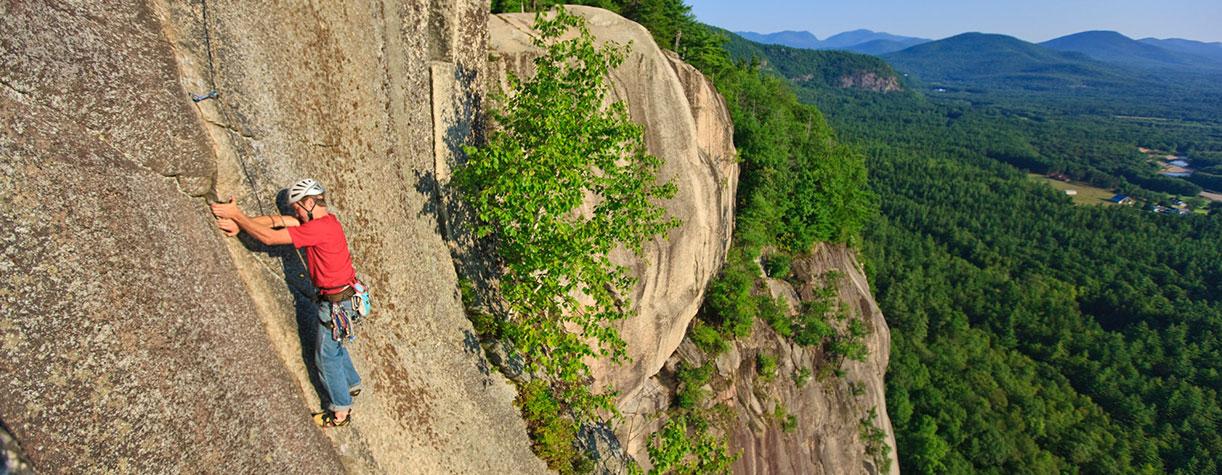 Person in red shirt rock climbing steep rock face