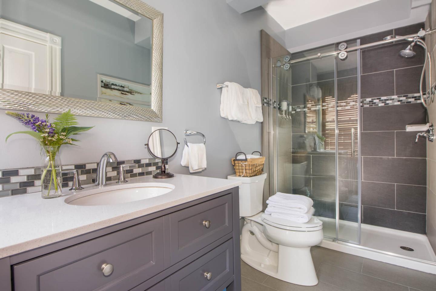 Full size bathroom with vanity, toilet, and glass shower in light blue and grey.