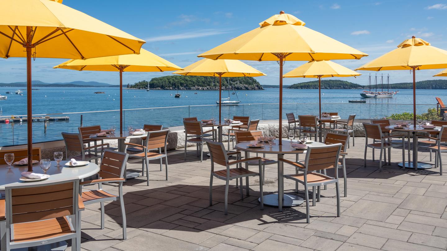 Outdoor dining at the Terrace Grille at the Bar Harbor Inn with views of the ocean and bright yellow umbrellas.