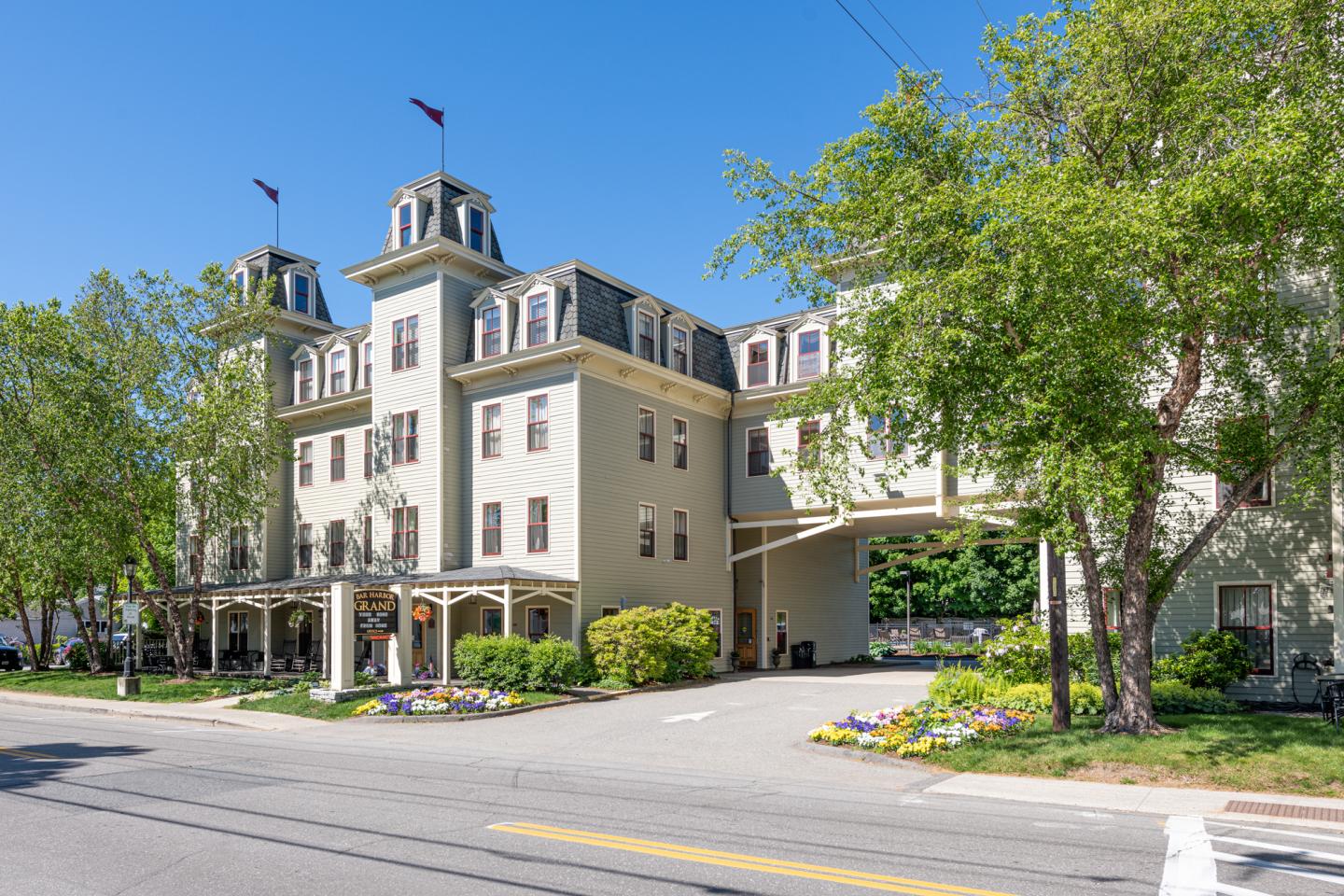 The four story Bar Harbor Grand Hotel sits in downtown Bar Harbor, with historic design elements including the portico for unloading baggage, long porch, and custom turrets.
