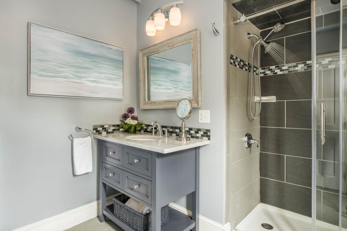 Full size bathroom with vanity, toilet, and glass shower in light blue and grey.