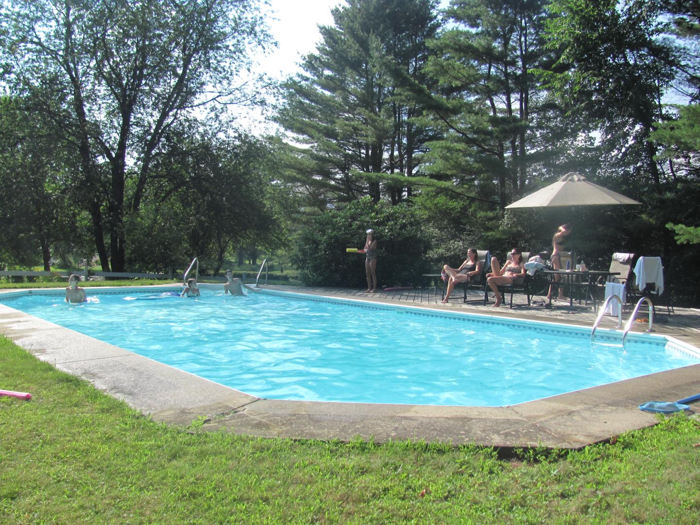 Outdoor in-ground pool with family gathering at tables.