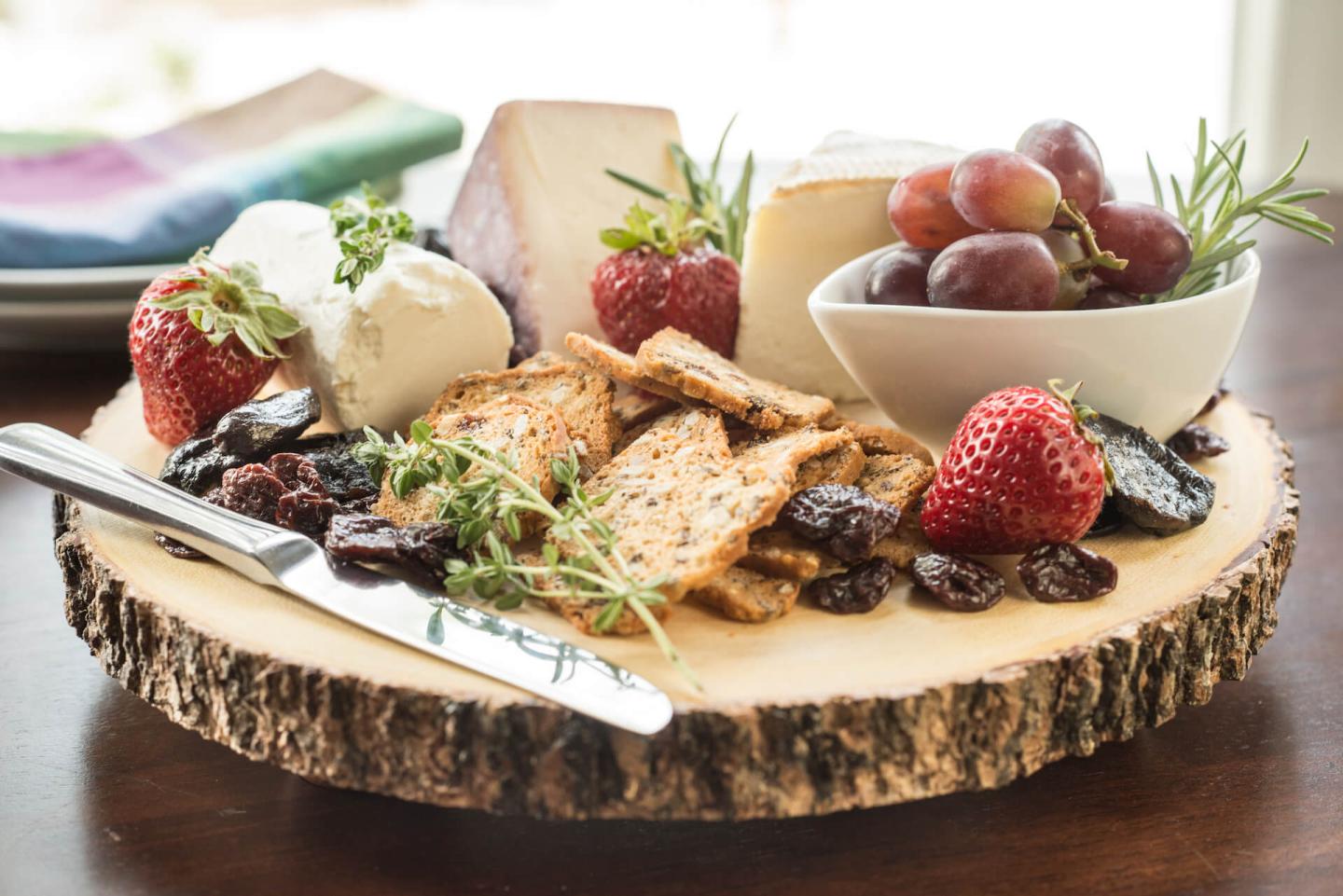 Rustic round platter topped with fresh cheese wedges, crackers, berries and grapes