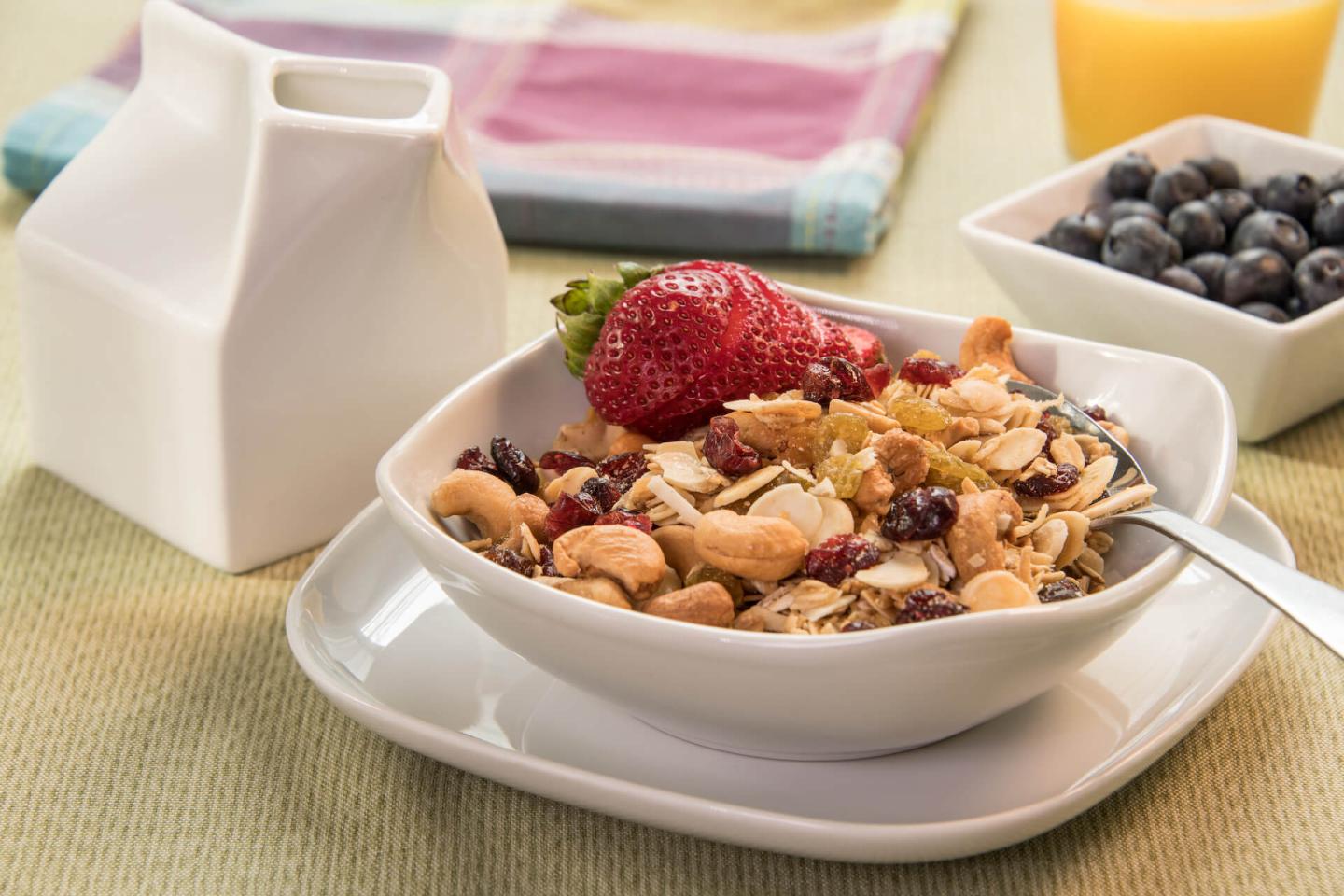 A white cereal bowl filled with house made granola with oats, almonds, dried cranberries, raisins, and golden raisins