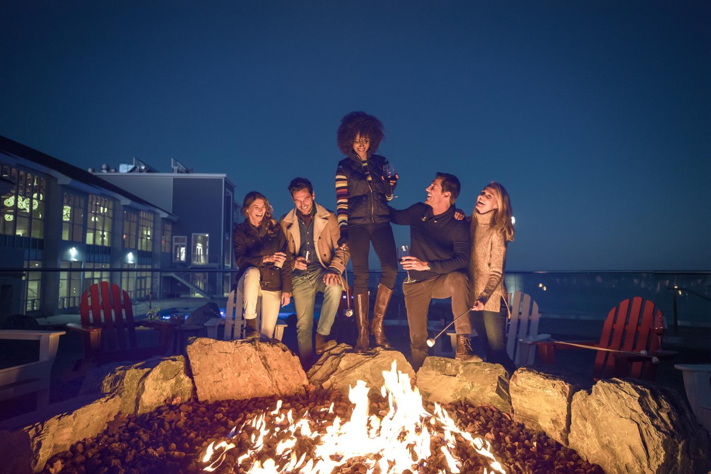 A group of people standing around a fire pit on the beach