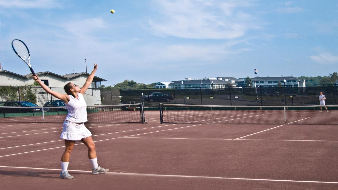 woman serves to man on Stage Neck Inn clay tennis courts
